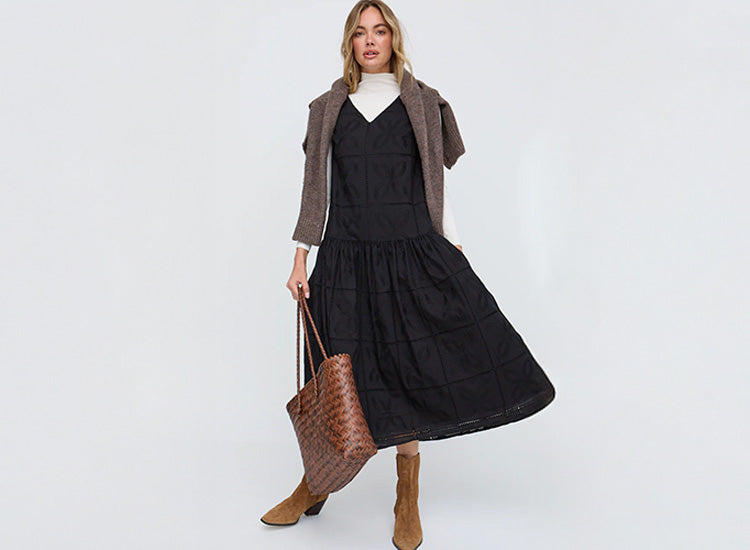 Woman wearing a black dress with a brown jacket and holding a brown bag on a white background