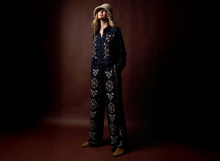 Person wearing a dark outfit with floral patterns against a brown background