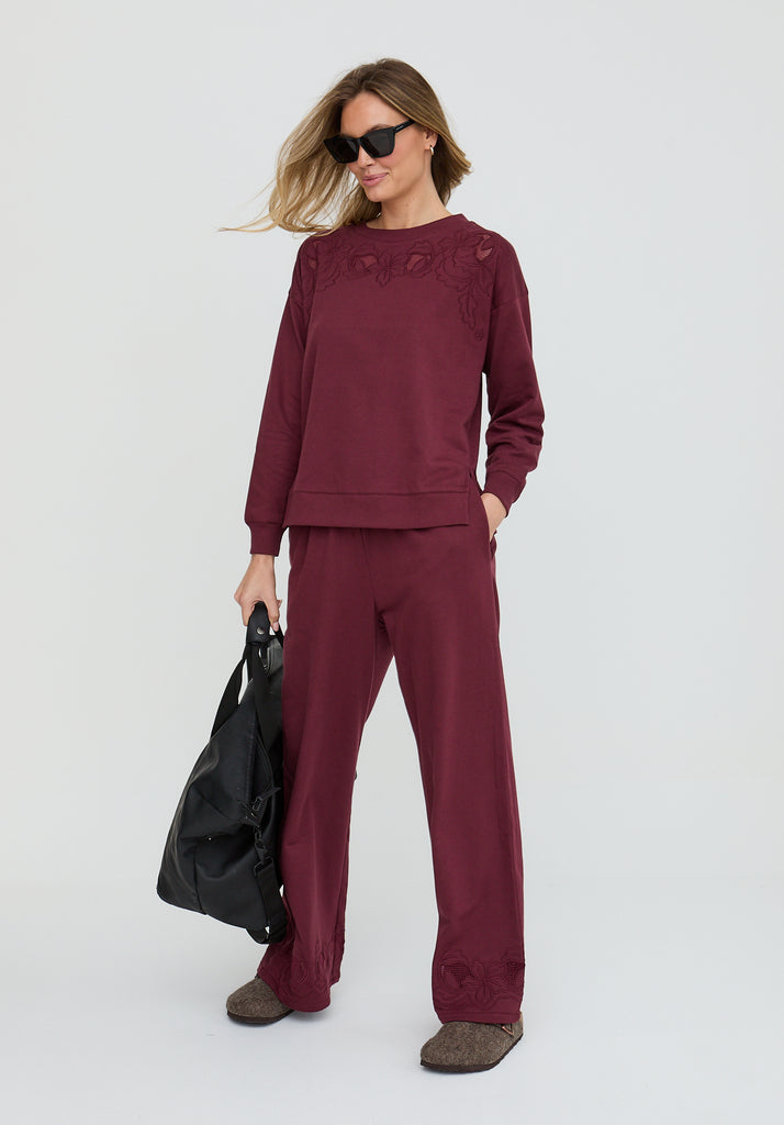 Woman wearing a burgundy outfit with sunglasses and holding a black bag on a white background