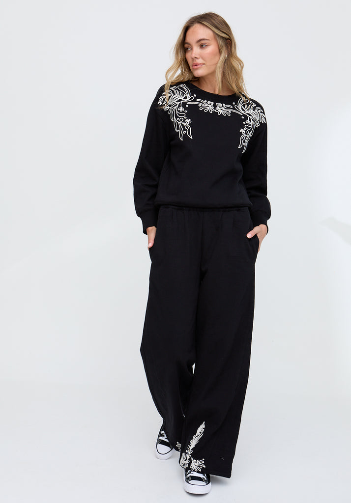 Woman wearing a black outfit with white embroidery on a white background