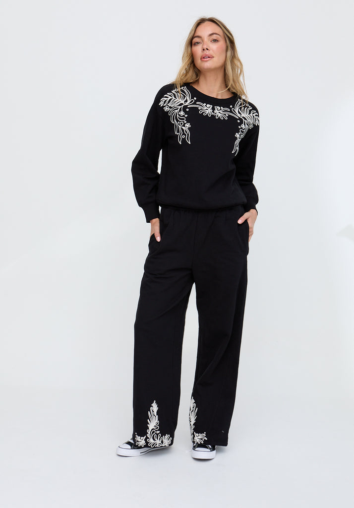 Woman wearing a black outfit with white embroidery on a white background