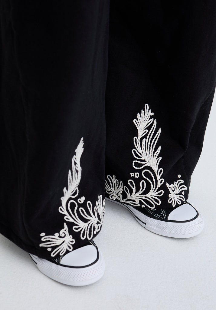 Black high-top sneakers with white floral patterns worn by a person.