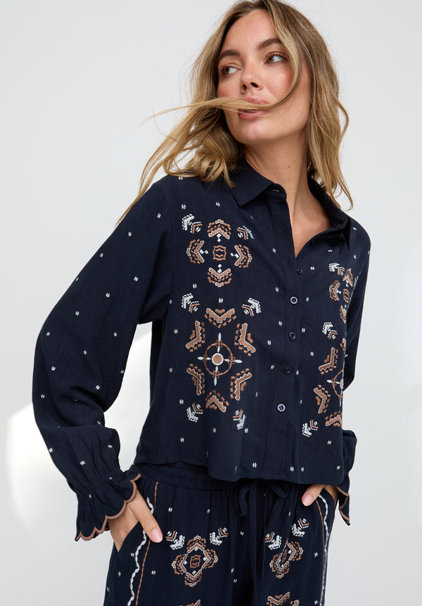 Woman wearing a navy blue embroidered shirt and pants on a white background