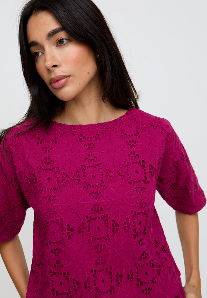 Woman wearing a pink lace dress against a plain background