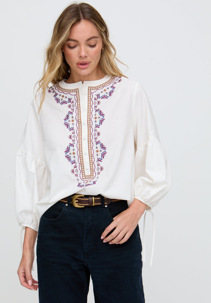 Woman wearing a white blouse with intricate embroidery on a plain background
