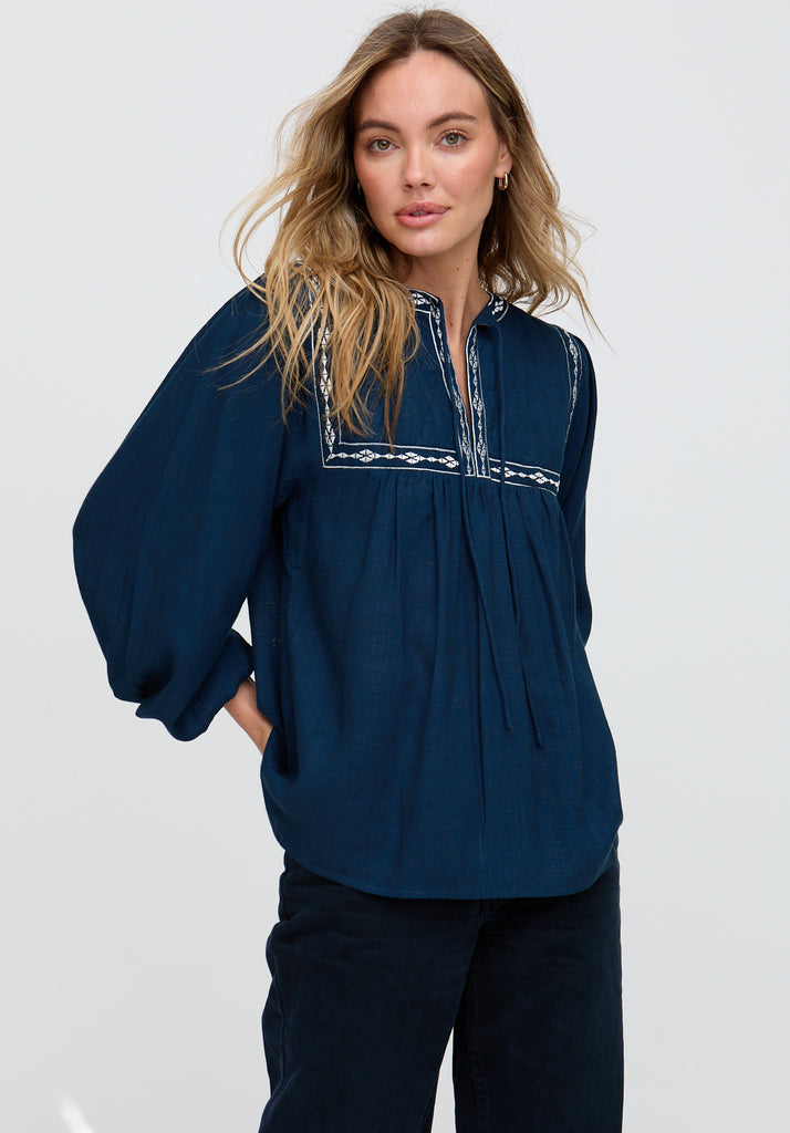 Woman wearing a navy blue blouse with embroidered details on a white background