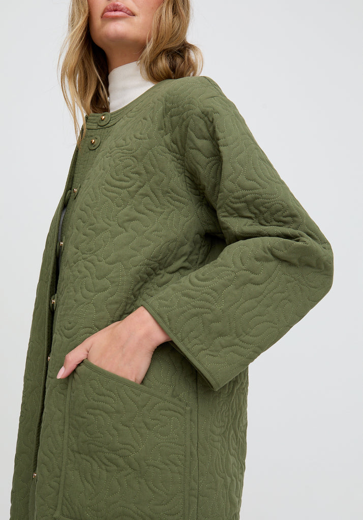 Green quilted coat worn by a person on a white background