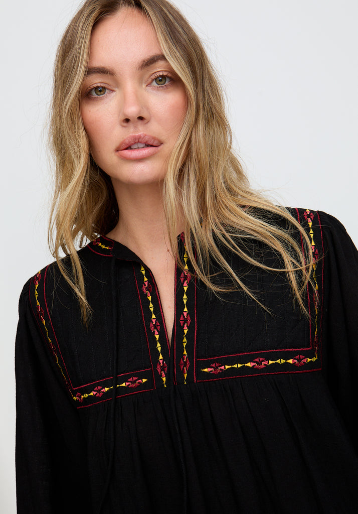 Woman wearing a black dress with colorful embroidery on a white background
