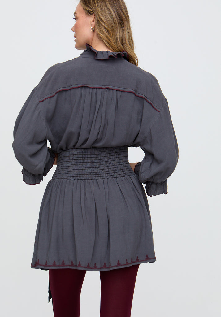 Woman wearing a gray dress with smocked waist and puffed sleeves on a light gray background