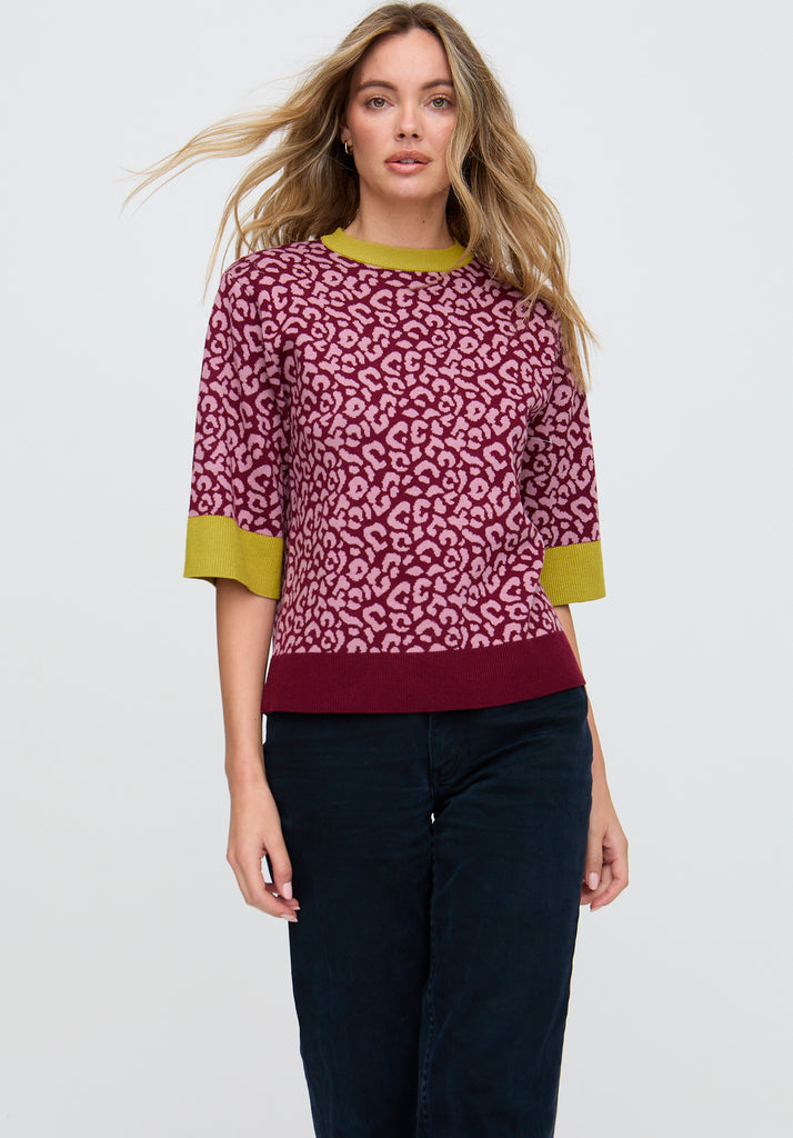 Woman wearing a pink leopard print sweater with green accents on a white background