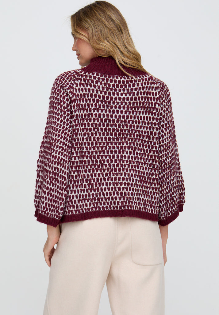 Woman wearing a patterned sweater and white pants on a plain background