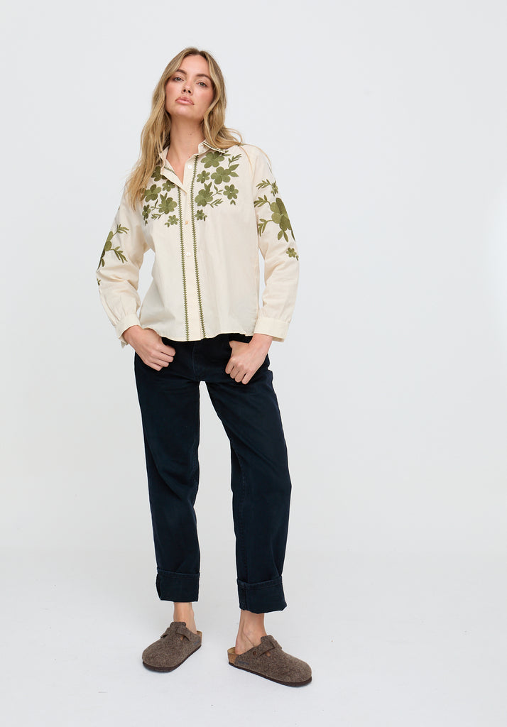 Woman wearing a floral shirt and dark pants on a white background