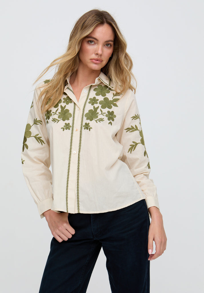 Woman wearing a cream blouse with green floral patterns on a white background