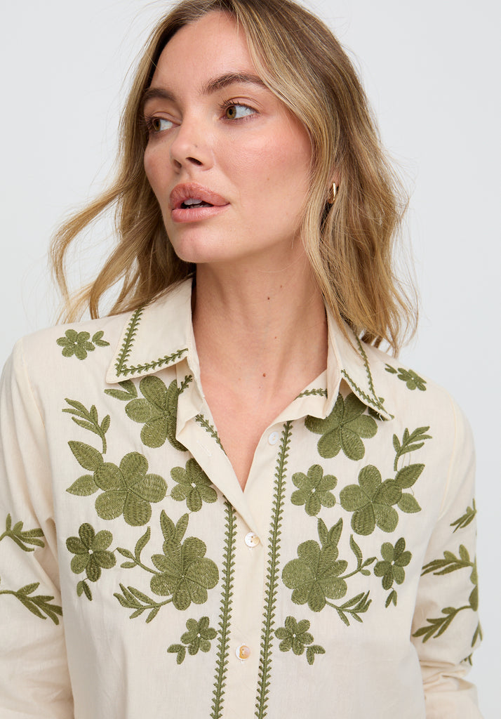 Woman wearing a cream blouse with green floral embroidery on a white background