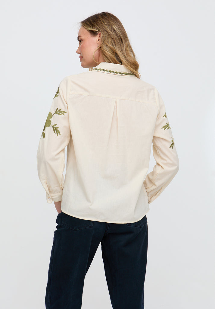 Woman wearing a beige blouse with green floral embroidery on a white background