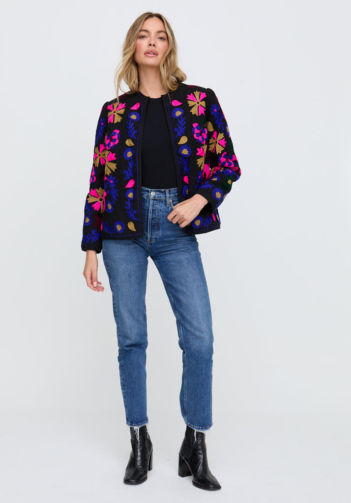 Woman wearing a colorful floral jacket, black top, blue jeans, and black boots on a white background