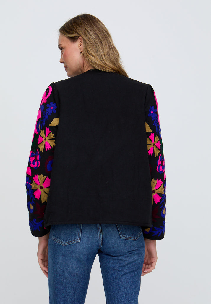 Person wearing a black jacket with colorful floral patterns on sleeves against a white background