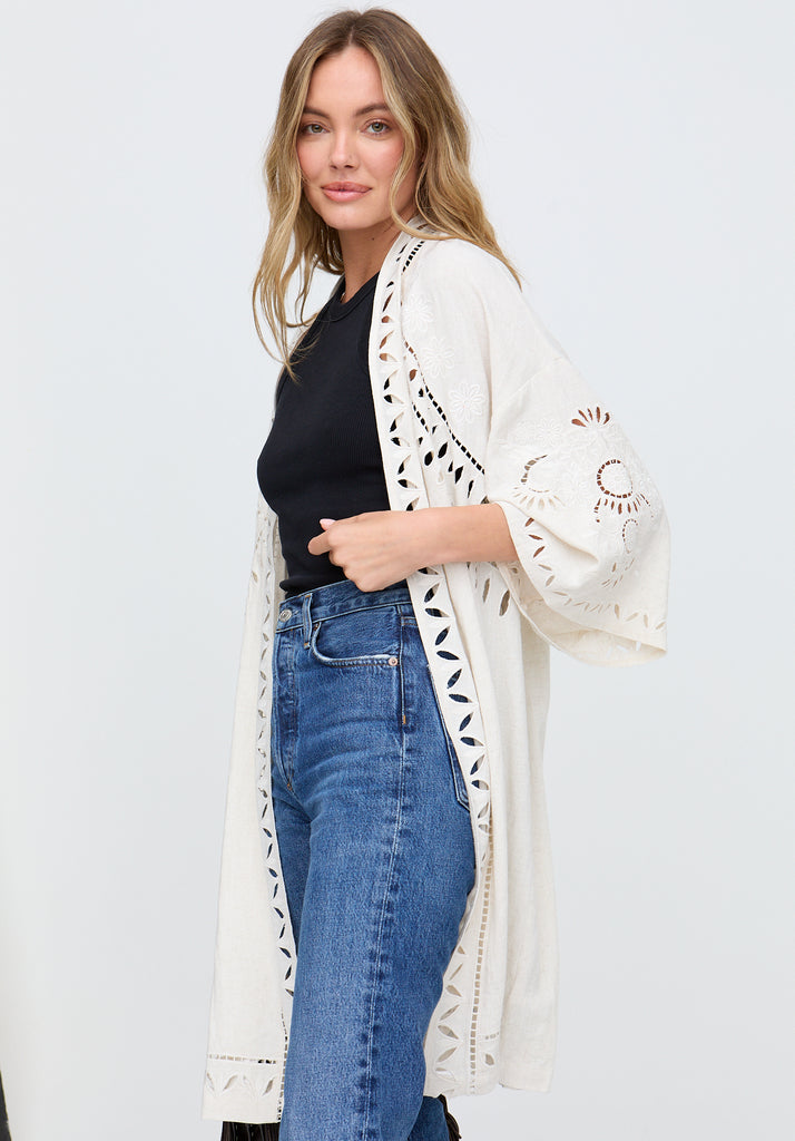 Woman wearing a white lace kimono over a black top and blue jeans on a white background