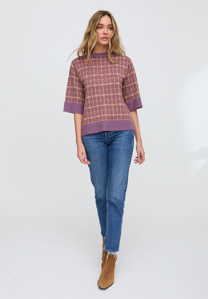 Woman wearing a patterned sweater and blue jeans on a white background