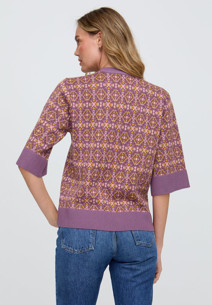 Woman wearing a patterned shirt with purple accents and blue jeans on a light gray background