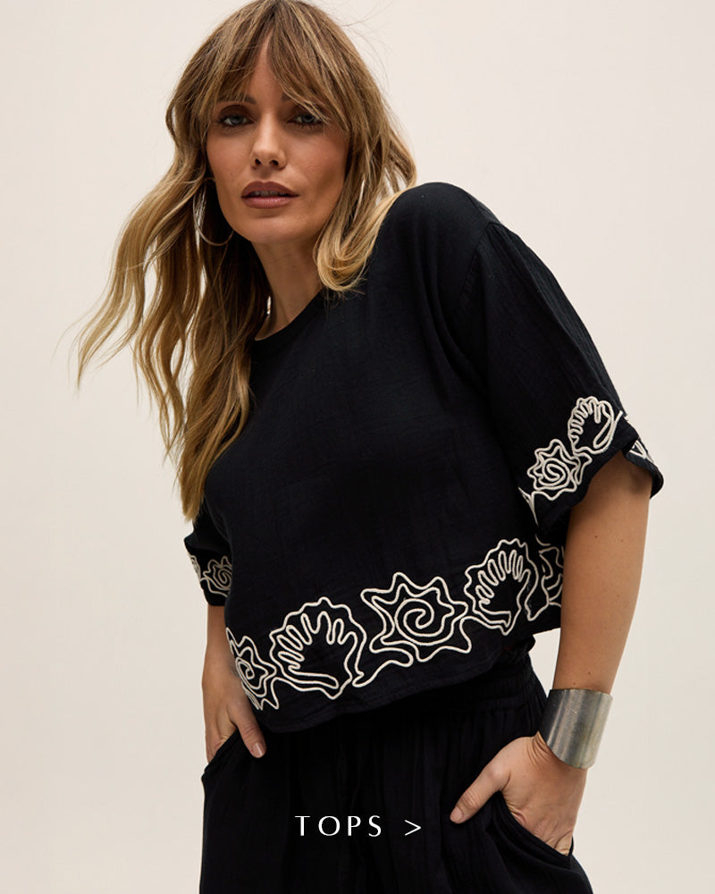 Model styles our Milly Embroidered Split Open Back Blouse In Black. Copy on image 'Tops - Shop Now'.