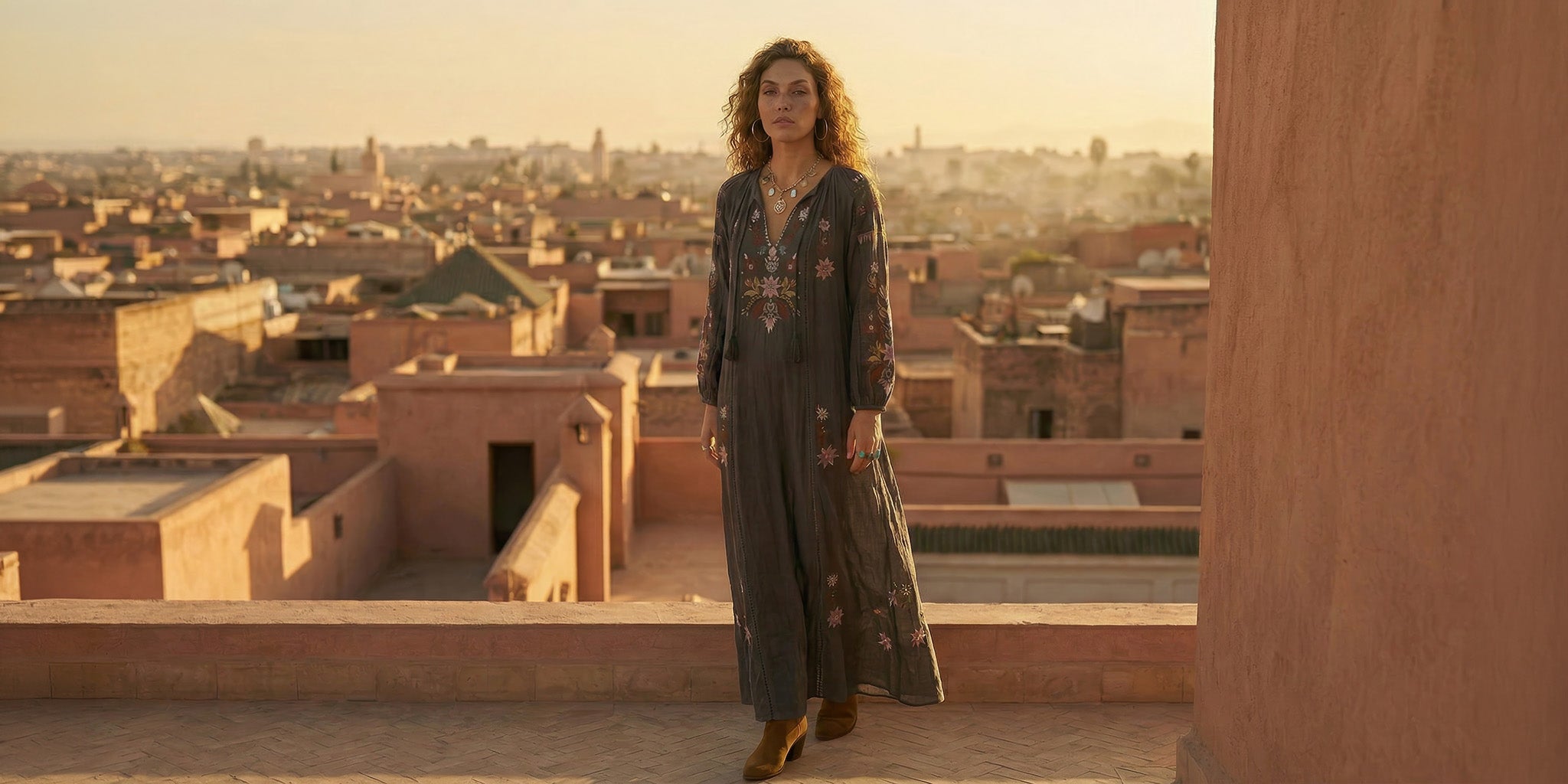Woman standing on a rooftop with a cityscape in the background during sunset.