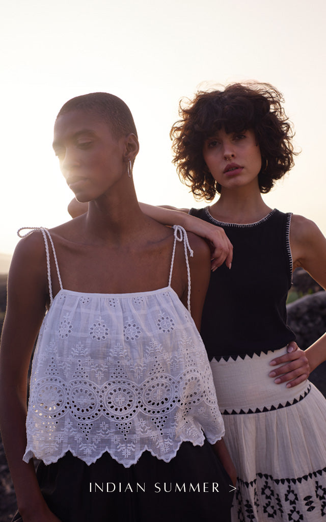 Model on left wearing white embroidered cami with tie detail on shoulders. Model on right wearing black sleeveless jersey top with stitching detail, and a cream mini skirt with black geometric embroidery. Copy on image 'Indian Summer'