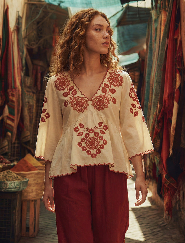 Woman wearing a white blouse with red embroidery and red pants in a market setting