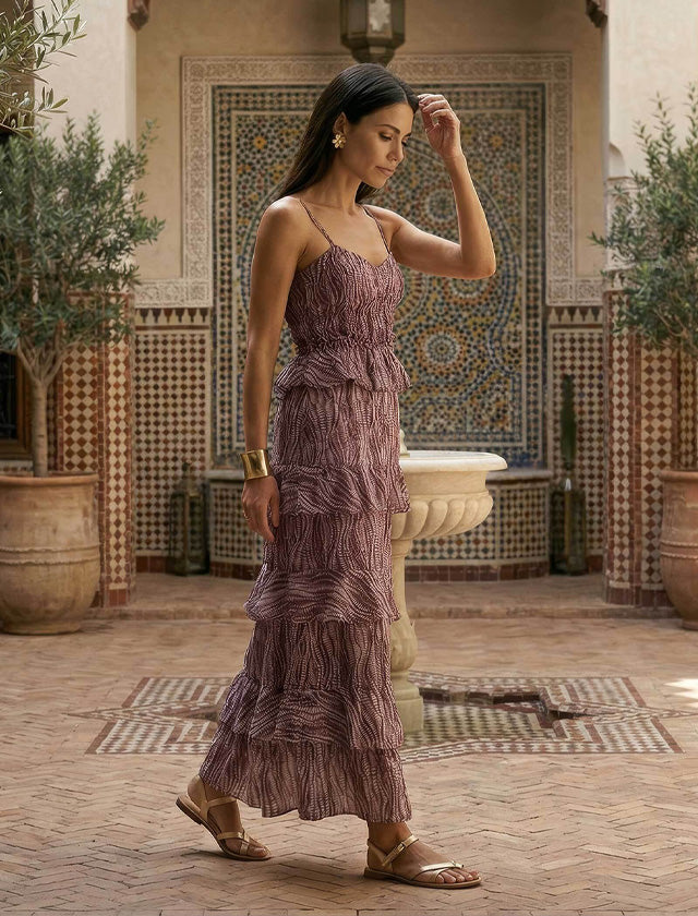 Woman in a purple dress standing in a courtyard with decorative tiles and plants.