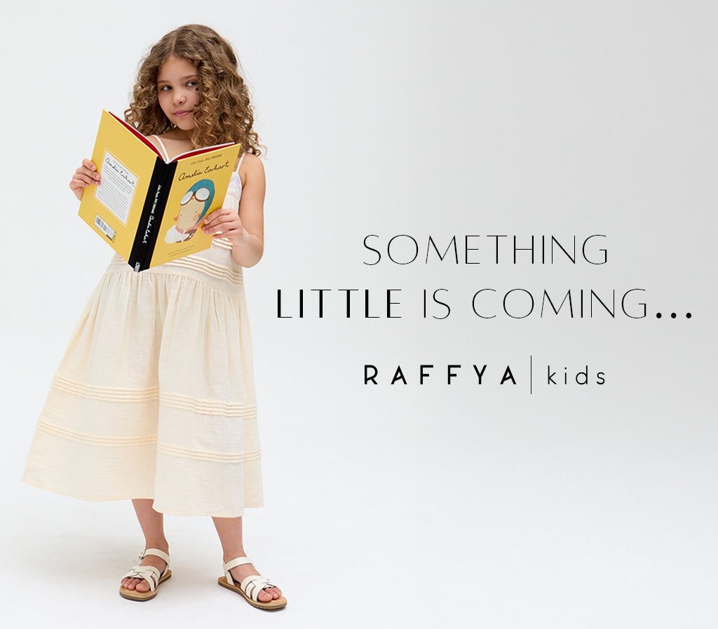Raffya Kids | Girls stands reading emelia earhart book whilst wearing raffya kids linen cream midi dress with embroidered detailing. 