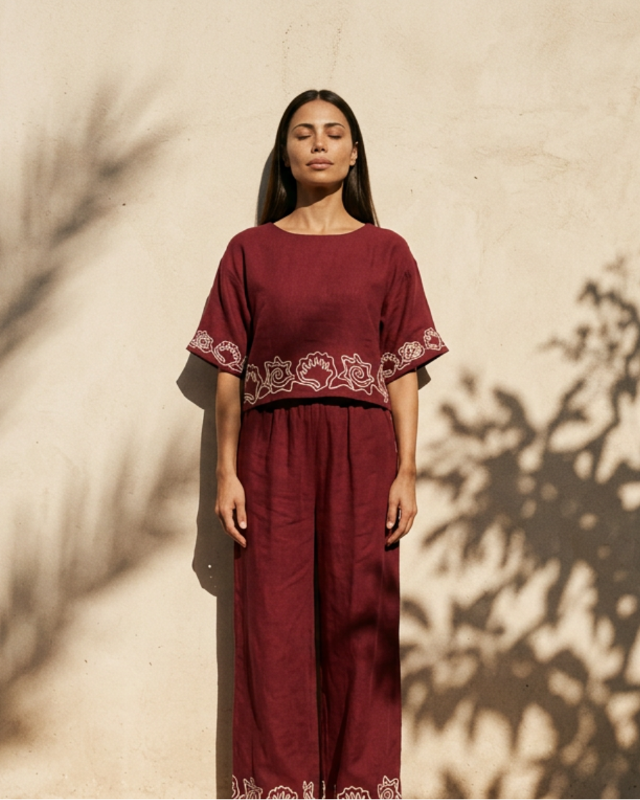 Woman wearing a burgundy outfit with embroidery against a beige wall