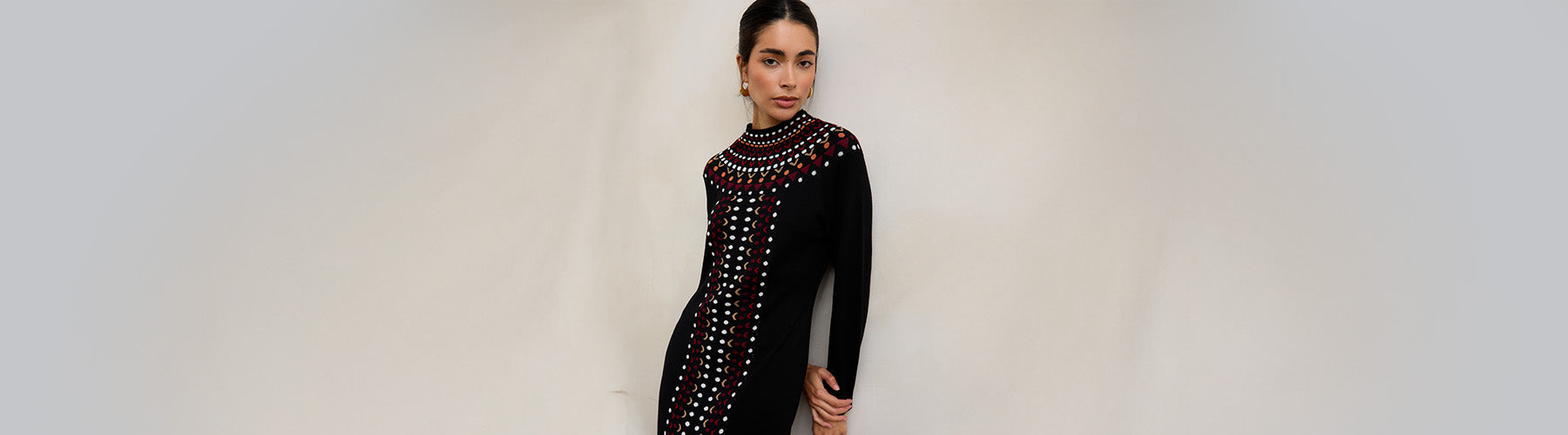 Woman wearing a black dress with red and gold embellishments against a plain background