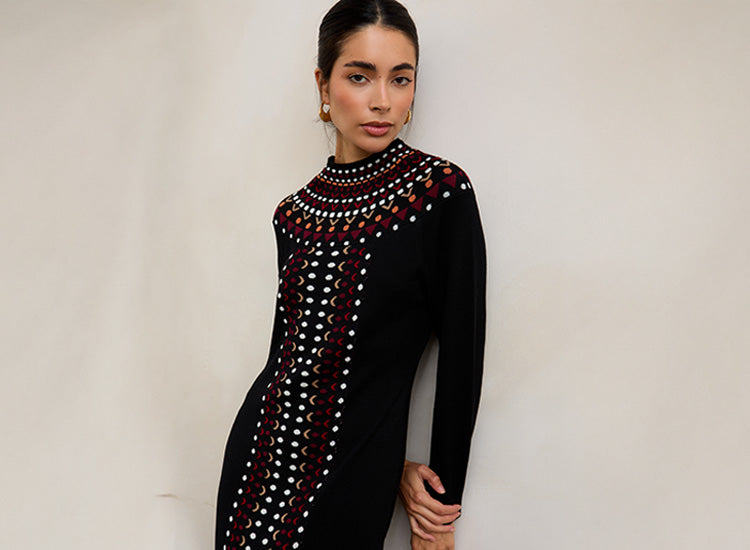 Woman wearing a black dress with colorful patterns against a plain background